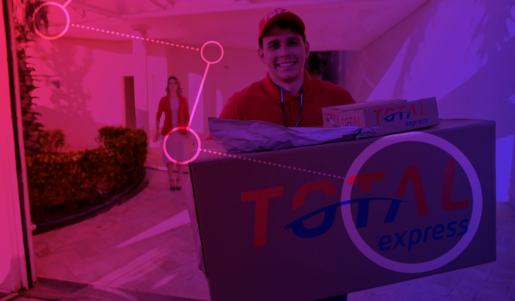 Imagem de homem com o uniforme da Total Express segurando uma caixa de papelão grande com o logotipo da empresa. Ao fundo uma mulher parada