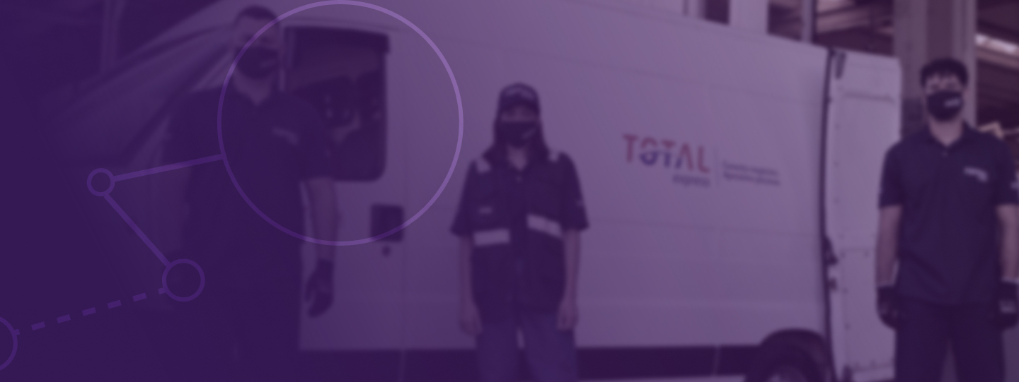 Foto de três pessoas com o uniforme da Total Express olhando para a câmera com os braços ao lado do corpo. Ao fundo uma van com o logotipo da empresa com as portas traseiras abertas